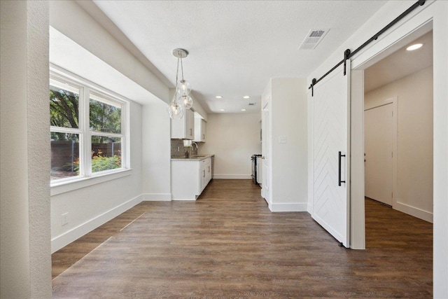 2701 Coatbridge Dr, Austin, TX 78745 - kitchen with a barn door, white cabinets, dark wood-style flooring, recessed lighting, and decorative light fixtures