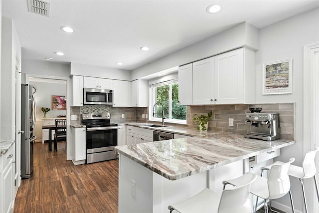 7314 Danwood Dr, Austin, TX 78759 - kitchen with stainless steel appliances, a peninsula, light stone counters, white cabinets, and recessed lighting