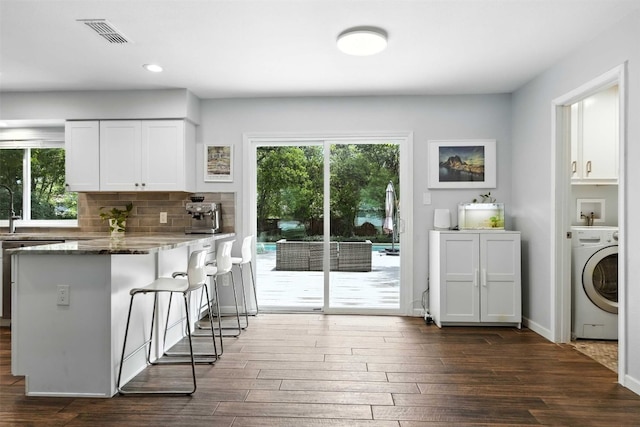 7314 Danwood Dr, Austin, TX 78759 - kitchen with washer / clothes dryer, dark wood-style flooring, a kitchen bar, white cabinetry, and decorative backsplash