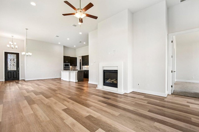 181 Benedum Way, Liberty Hill, TX 78642 - unfurnished living room with a towering ceiling, a chandelier, ceiling fan, a glass covered fireplace, and light wood-style floors