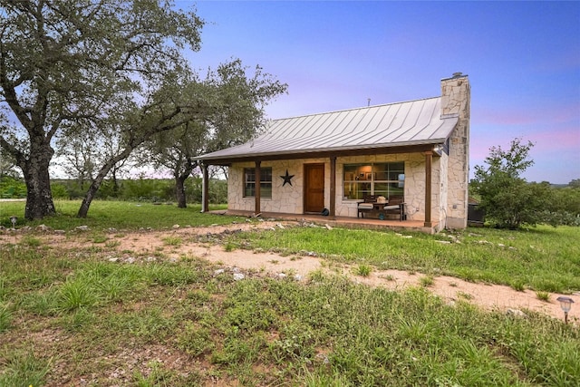 24205 State Highway 71 W, Spicewood, TX 78669 - back of house at dusk featuring stone siding, a standing seam roof, a chimney, a metal roof, and covered porch