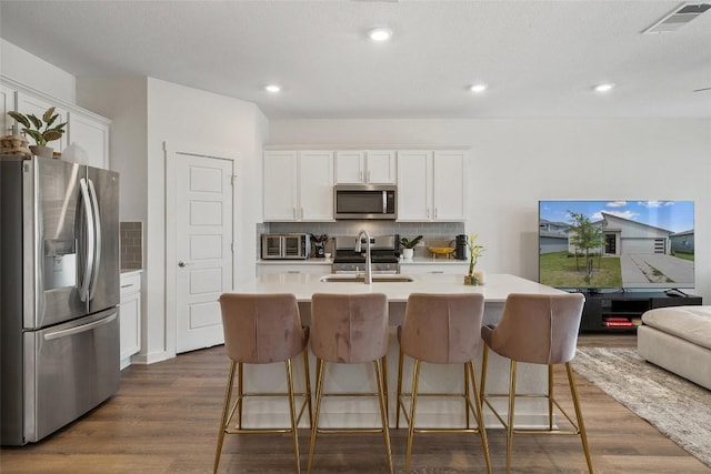 13821 Zuhause Dr, Pflugerville, TX 78660 - kitchen featuring stainless steel appliances, tasteful backsplash, white cabinets, light countertops, and a center island with sink