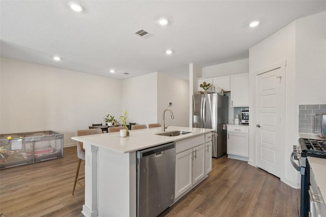 13821 Zuhause Dr, Pflugerville, TX 78660 - kitchen featuring appliances with stainless steel finishes, wood finished floors, a center island with sink, a breakfast bar, and white cabinets