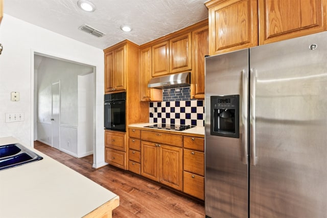8511 Slant Oak Dr, Austin, TX 78729 - kitchen featuring black appliances, light countertops, decorative backsplash, wood finished floors, and under cabinet range hood