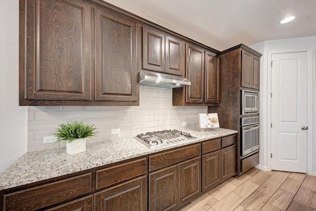 2953 Diego Dr, Round Rock, TX 78665 - kitchen featuring backsplash, dark brown cabinetry, stainless steel appliances, under cabinet range hood, and light stone counters
