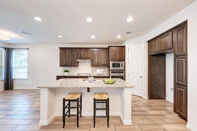 2953 Diego Dr, Round Rock, TX 78665 - kitchen featuring tasteful backsplash, a kitchen island with sink, dark brown cabinetry, a breakfast bar, and appliances with stainless steel finishes