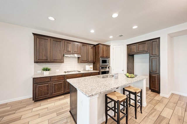 2953 Diego Dr, Round Rock, TX 78665 - kitchen featuring wood tiled floors, tasteful backsplash, dark brown cabinetry, an island with sink, and a breakfast bar