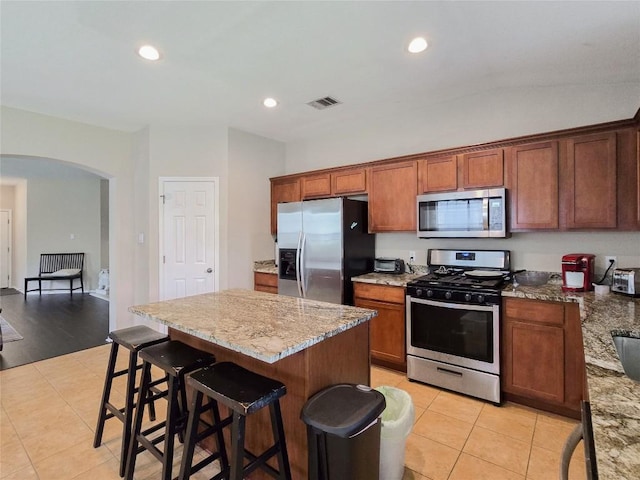 11704 Fletcher Hall Ln, Austin, TX 78717 - kitchen with appliances with stainless steel finishes, arched walkways, light tile patterned floors, light stone counters, and a breakfast bar