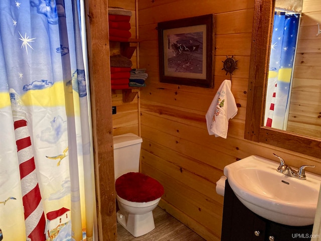 bathroom with toilet, wood-type flooring, vanity, and wood walls