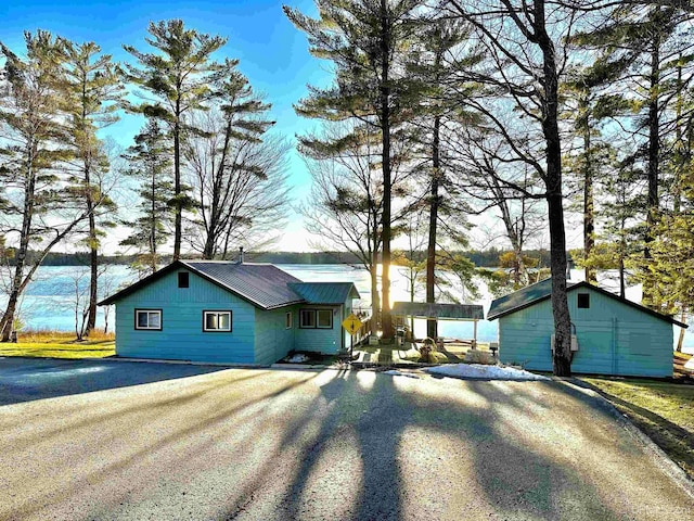 view of front facade featuring metal roof, driveway, and an outbuilding