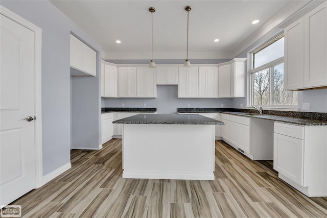 kitchen with white cabinetry, light wood-type flooring, dark stone countertops, a center island, and pendant lighting