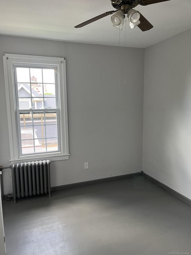 spare room featuring radiator, concrete flooring, ceiling fan, and plenty of natural light