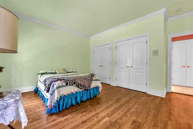 bedroom featuring two closets, ornamental molding, and hardwood / wood-style flooring