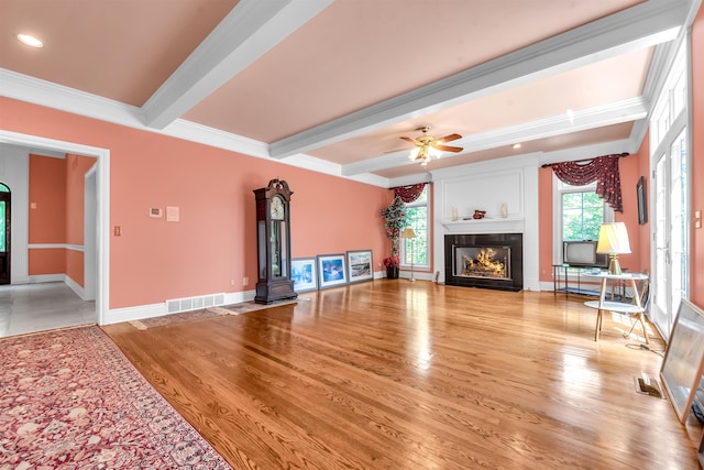 unfurnished living room featuring beam ceiling, light hardwood / wood-style floors, ornamental molding, and ceiling fan