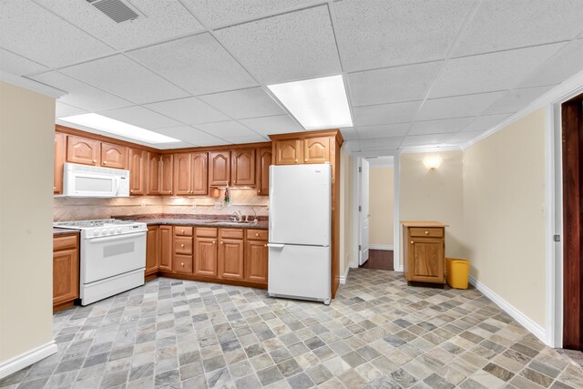 kitchen with white appliances, backsplash, light tile flooring, and a paneled ceiling