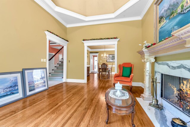 living area with a tray ceiling, hardwood / wood-style floors, crown molding, a fireplace, and a notable chandelier