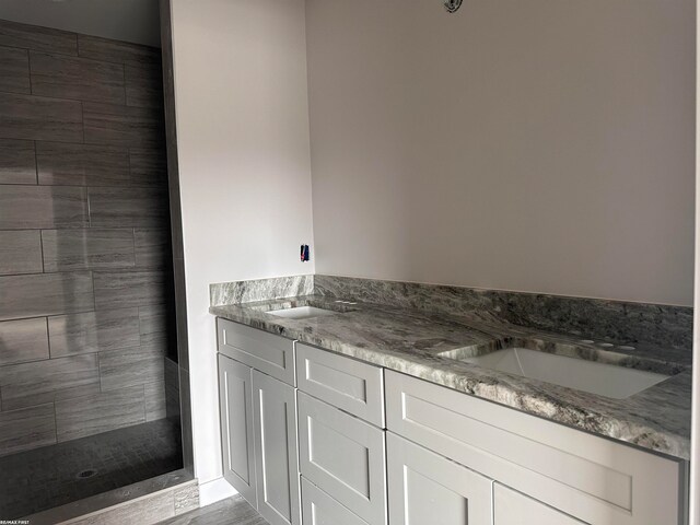 bathroom with double sink vanity and tiled shower