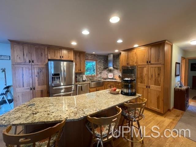 kitchen featuring a breakfast bar area, stainless steel appliances, light hardwood / wood-style floors, wall chimney exhaust hood, and sink