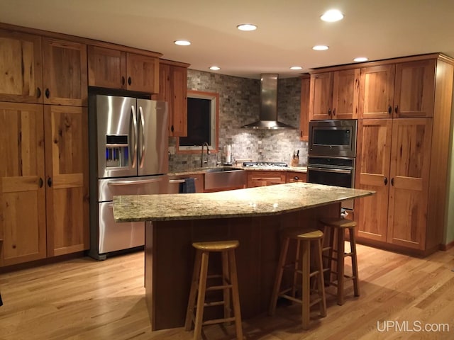 kitchen featuring stainless steel appliances, light hardwood / wood-style floors, light stone countertops, and wall chimney exhaust hood