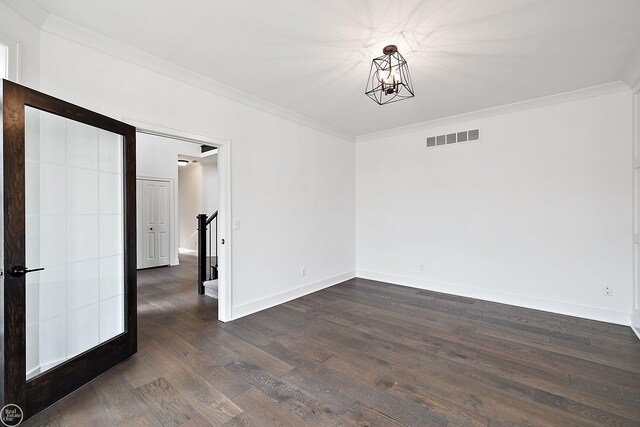 spare room with crown molding, a notable chandelier, visible vents, dark wood-type flooring, and baseboards