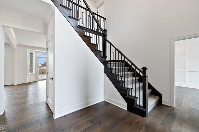 staircase featuring a high ceiling, crown molding, baseboards, and wood finished floors