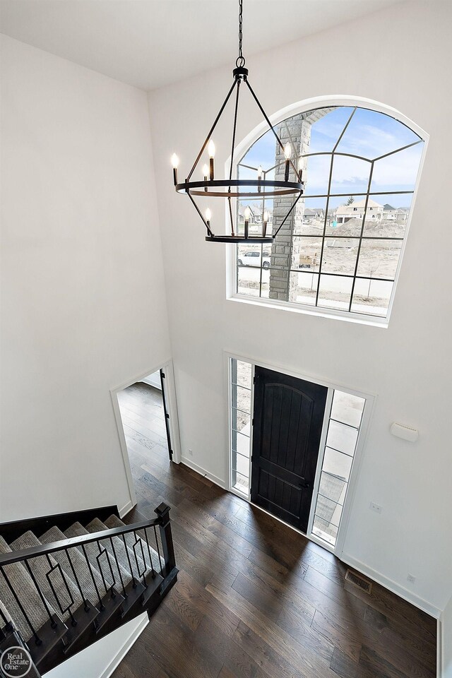 foyer featuring baseboards, visible vents, a towering ceiling, dark wood-type flooring, and an inviting chandelier