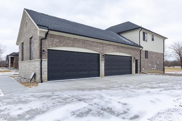 view of snow covered exterior with an attached garage, roof with shingles, and brick siding