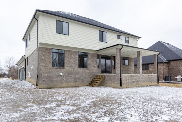 snow covered rear of property with covered porch, brick siding, and central air condition unit