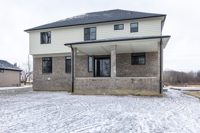 snow covered rear of property with brick siding