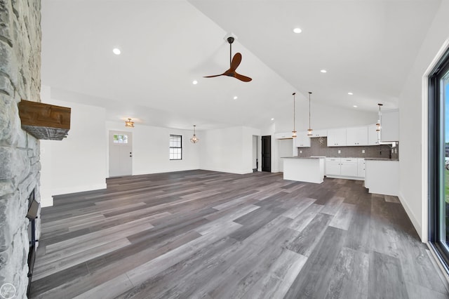 unfurnished living room featuring dark hardwood / wood-style flooring, a stone fireplace, ceiling fan, and lofted ceiling