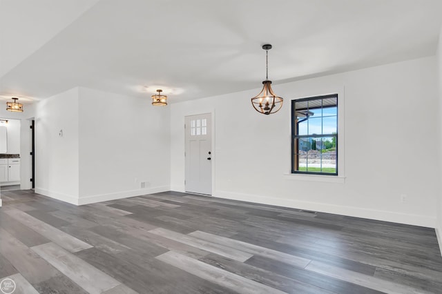 empty room featuring a notable chandelier and dark wood-type flooring