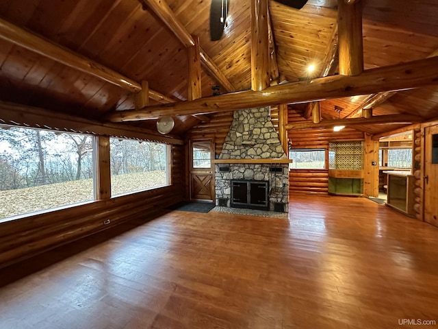 unfurnished living room featuring dark wood-type flooring, a stone fireplace, rustic walls, and lofted ceiling with beams