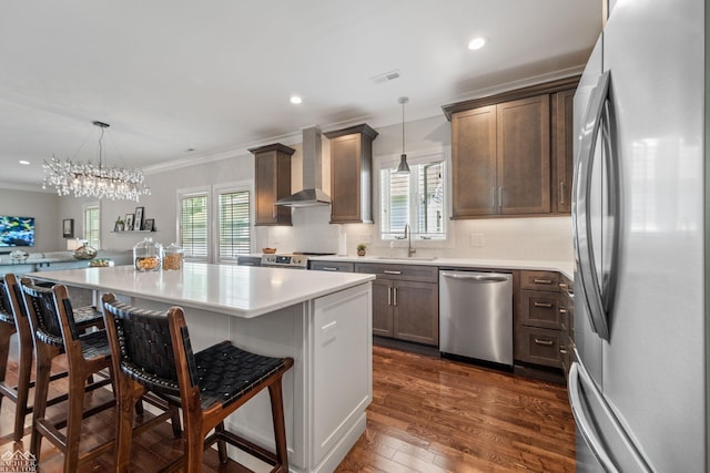 kitchen featuring decorative light fixtures, sink, a breakfast bar area, stainless steel appliances, and wall chimney range hood