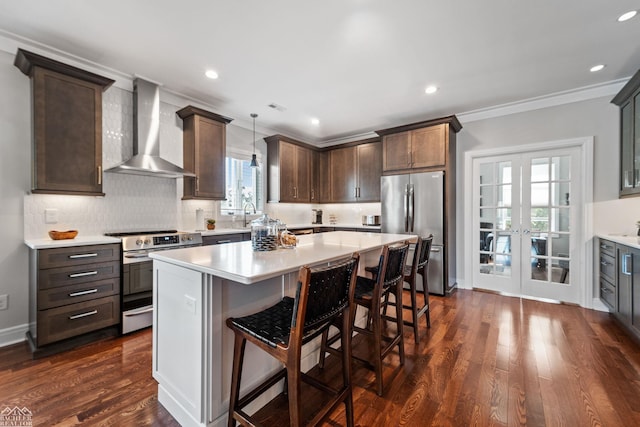 kitchen featuring appliances with stainless steel finishes, a breakfast bar, decorative light fixtures, a center island, and wall chimney exhaust hood