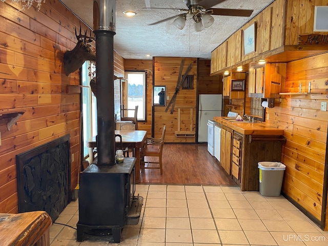 kitchen with wood walls, ceiling fan, a wood stove, and light hardwood / wood-style floors