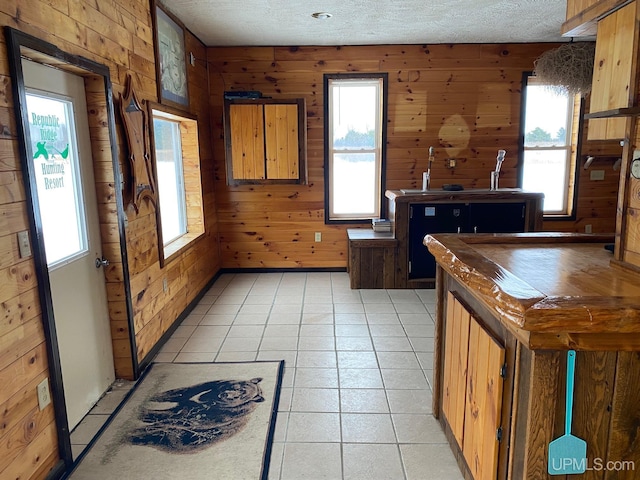 kitchen with wood walls, light tile patterned floors, and a textured ceiling