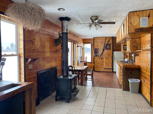 kitchen featuring ceiling fan, light tile patterned floors, a wood stove, and wooden walls