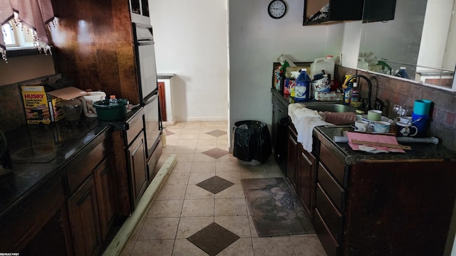 kitchen with multiple ovens, light tile patterned floors, dark brown cabinetry, and sink