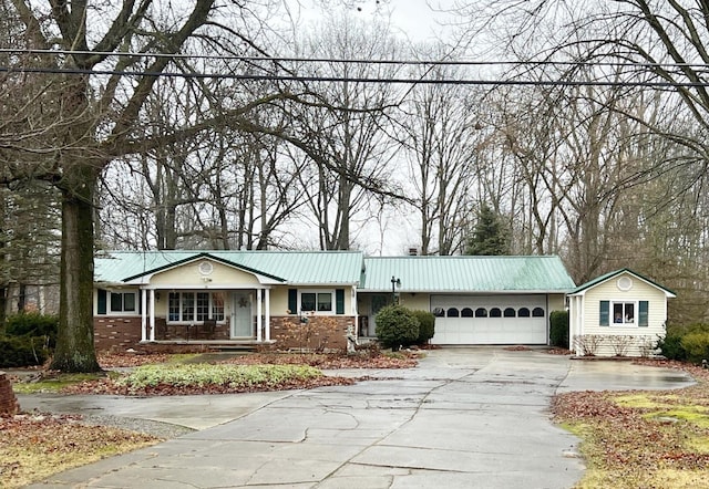 ranch-style house with driveway, metal roof, an attached garage, a porch, and brick siding