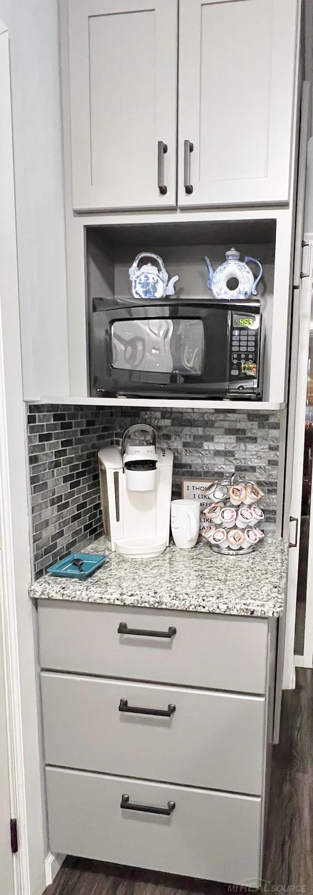 bar featuring black microwave, decorative backsplash, and dark wood-type flooring