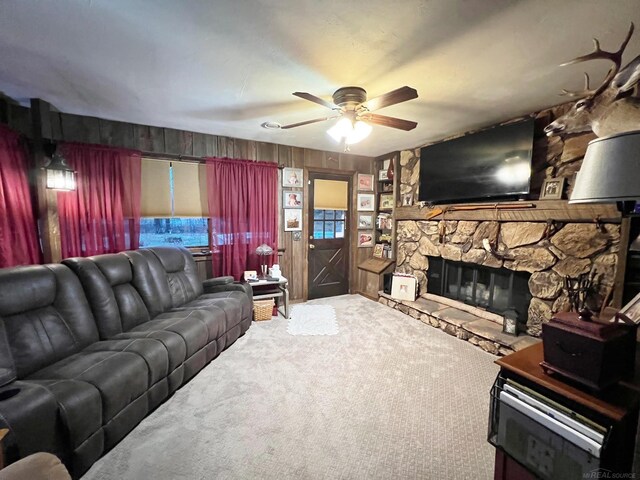 carpeted living room with ceiling fan and a stone fireplace