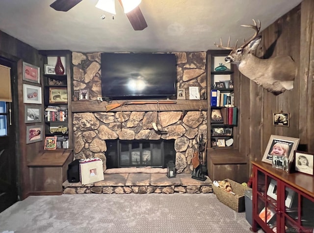 carpeted living room with a ceiling fan and a stone fireplace