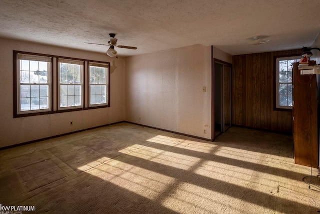 carpeted spare room featuring wooden walls, a textured ceiling, ceiling fan, and plenty of natural light