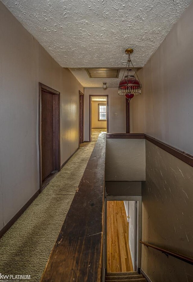 hallway with a tray ceiling, light carpet, and a textured ceiling