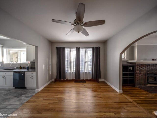 unfurnished living room with ceiling fan, sink, a brick fireplace, and light tile patterned floors