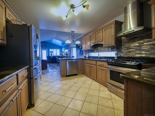 kitchen featuring wall chimney range hood, vaulted ceiling, appliances with stainless steel finishes, tasteful backsplash, and a chandelier