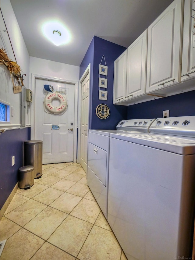 clothes washing area featuring washing machine and dryer, light tile patterned flooring, and cabinets