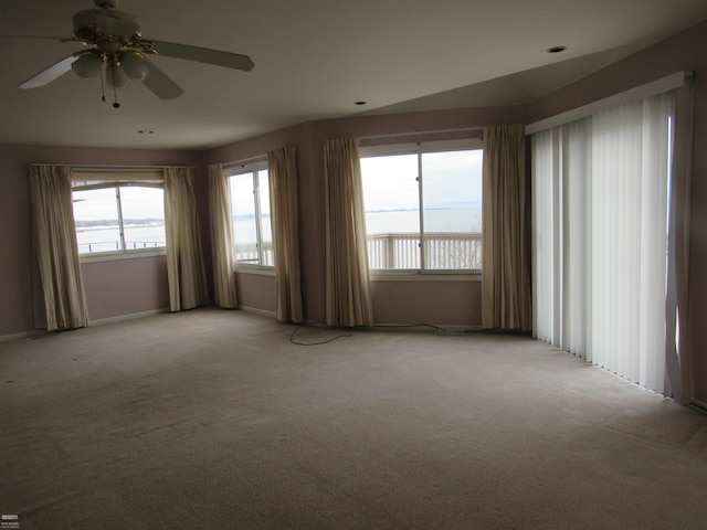 unfurnished room featuring a water view, light carpet, and ceiling fan