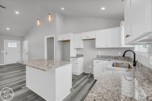 kitchen with white cabinets, light stone counters, a kitchen island, and sink