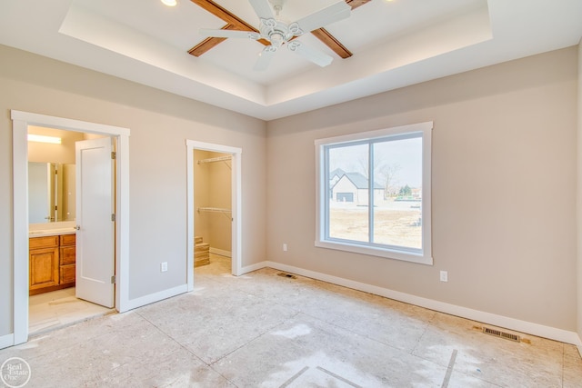 unfurnished bedroom featuring ceiling fan, a closet, a spacious closet, a raised ceiling, and connected bathroom